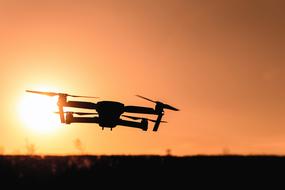 Drone with camera over dark land at sunset sky