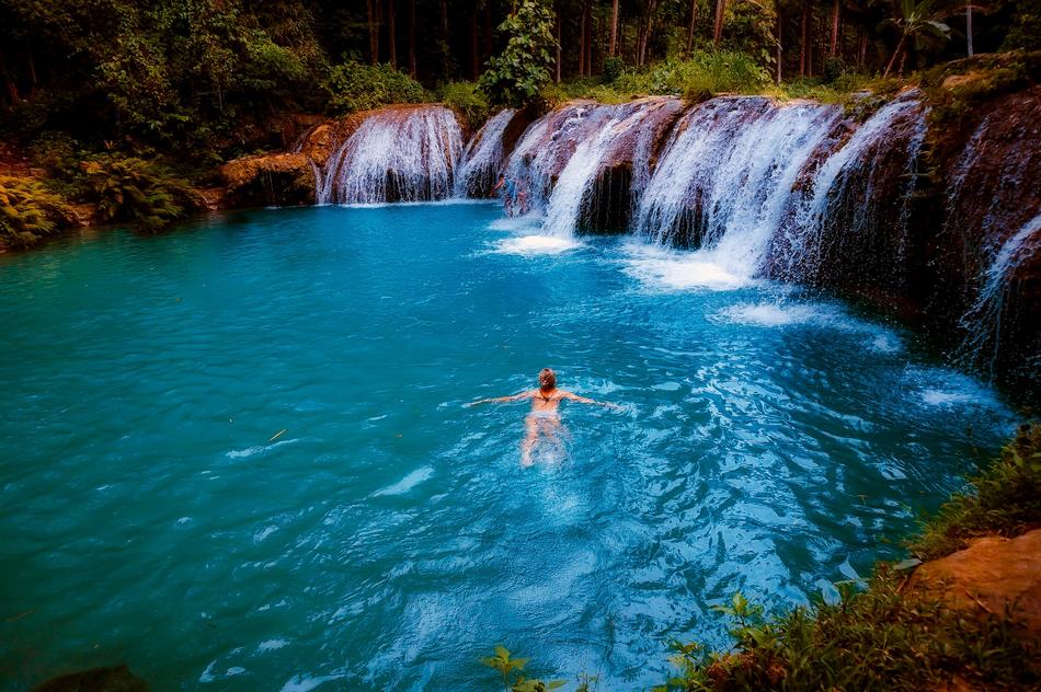 Girl swimming in the beautiful lake with waterfall among the colorful plants, on landscape