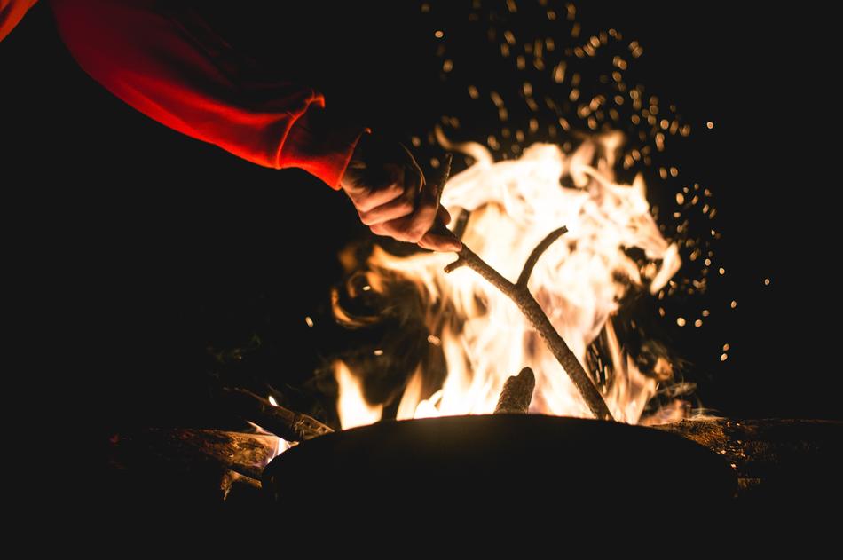 man with stick in hand near campfire at night