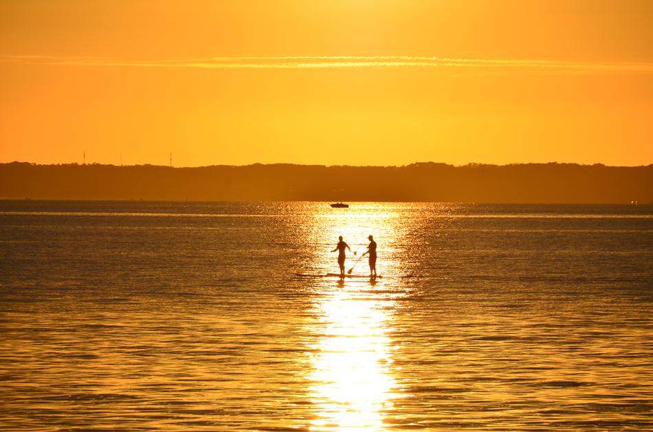 two persons with paddles on boat at sunrise