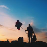 Silhouette of man with bunch of Balloons and backpack in front of city at Sunrise