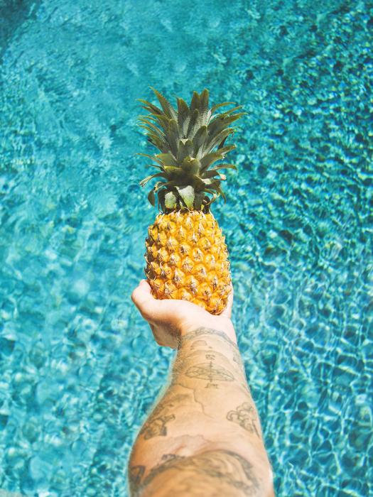pineapple in hand over swimming pool