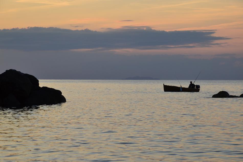 man fishing in boat near coast at sunset