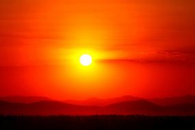 Sunset, white Solar disk at Red sky over mountains