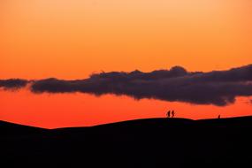 People walking on a rock against an orange sky