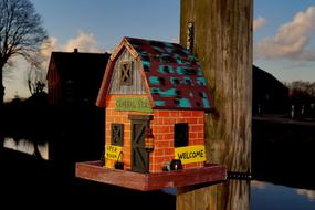 the colored bird house by the pole