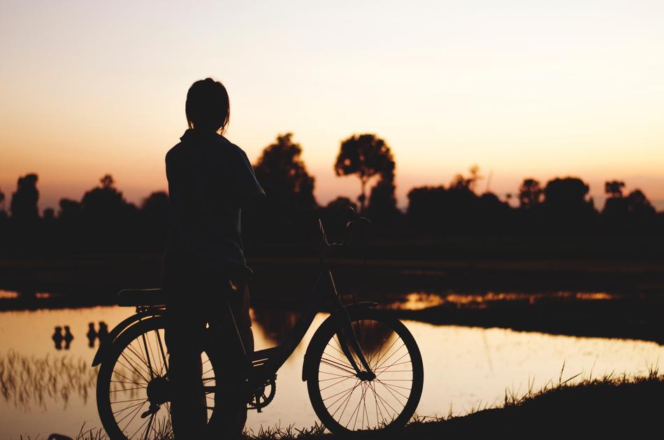 Silhouette of a girl with a bicycle near a lake