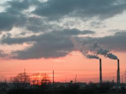 chimneys with grey smoke in City ​​at Sunset Sky