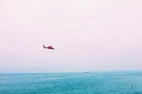 red helicopter flying over Blue sea