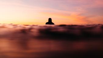 man swims away in sea at sunset