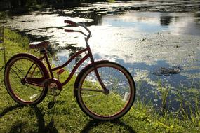 vintage red ladies bike standing on grass near water