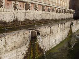 ancient roman fountain with head sculptures, italy