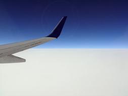 photo of an airplane wing against a background of white clouds and blue sky