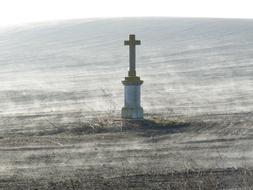 aged stone cross on plowed field