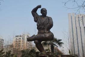 Bronze statue of the posing man among the trees and buildings
