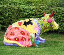multi-colored sculpture of a cow on a lawn in a park