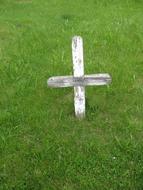 White cross on the grave among the green grass