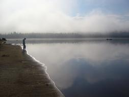 a man stands on the shore of a misty lake