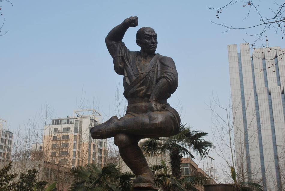 Bronze statue of the posing man among the trees and buildings