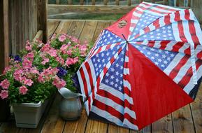 Beautiful and colorful flowers in the pots and umbrella with the flag of USA, on the wooden surface