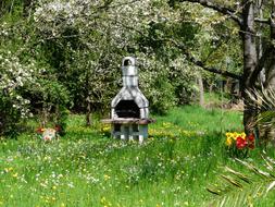 Beautiful grill, among the green meadow with colorful flowers and trees in spring