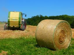 Green and yellow tractor and bale of straw on the beautiful and colorful field, at blue sky on background