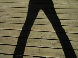 shadow of a man's feet on a wooden pier