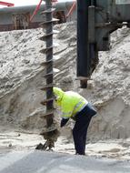 Person in bright, green jacket, drilling sand with the drill