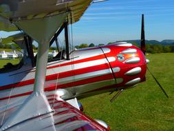 Close-up of the shiny, silver and red aircraft, on the green field, with the trees