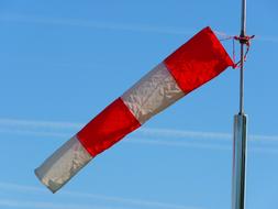 Red and white wind sock on the anemometer, in the airport, under the blue sky with clouds