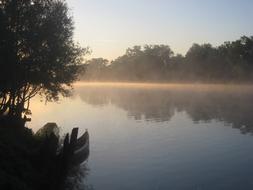 Beautiful waterscape of the Kupa river, with the boats, in deep mist, among the trees, at colorful and beautiful sunrise