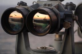 View of the shore, with the flying helicopter, at beautiful and colorful sunset, though the binoculars