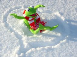 Cute and beautiful, green Kermit Frog in the red and white scarf, on the beautiful heart shape in the snow, in the winter