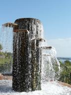 Beautiful fountain, with the round steps, among the colorful plants, under the blue sky with clouds