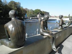 Shiny sculptures of the people, near the river in Berlin, Germany, among the plants