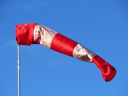 Close-up of the red and white, striped wind direction indicator in sunlight, at blue sky on background