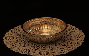 Beautiful, shiny, silver bowl on the patterned towel, at dark background