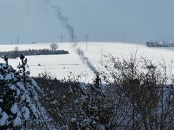 Landscape with the plants, smoke and power lines, in snow, in the winter