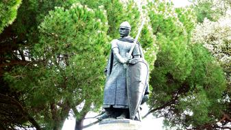 Statue of the knight with sword and shield near the beautiful, green trees in sunlight, in Lisbon, Portugal