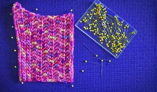 Colorful crochet hat and yellow pins with the box, on the blue surface