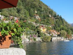 Beautiful landscape of the lake coast with colorful buildings and plants, on the mountains, in sunlight, under the blue sky