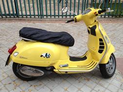 Shiny, yellow and black scooter on the pavement, near the fence