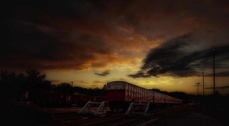 Train on the railway, among the plants, at beautiful and colorful sunset, with the clouds
