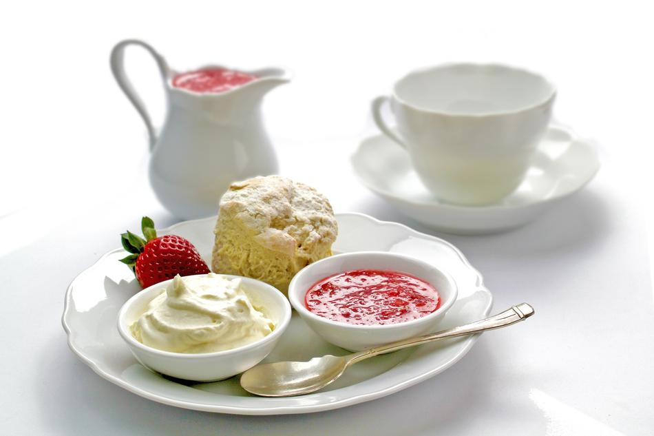 Beautiful muffin, strawberry sauce, cream and red strawberry on the plate, near the cup and jug