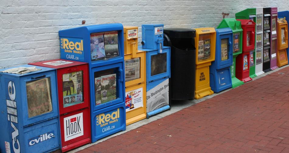 row of multi-colored vending machines selling newspapers at wall