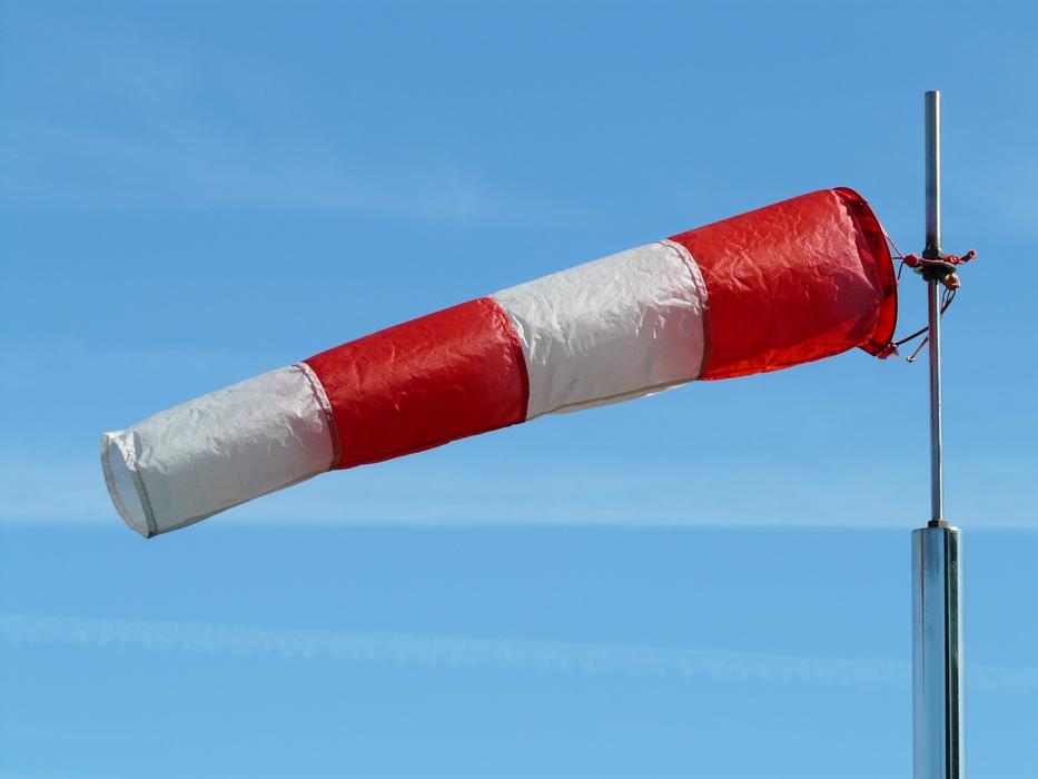 Red and white, shiny windsock, on the pole, at blue sky with clouds on background