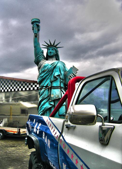 Replica of the Statue of Liberty, near the colorful car, under the cloudy sky