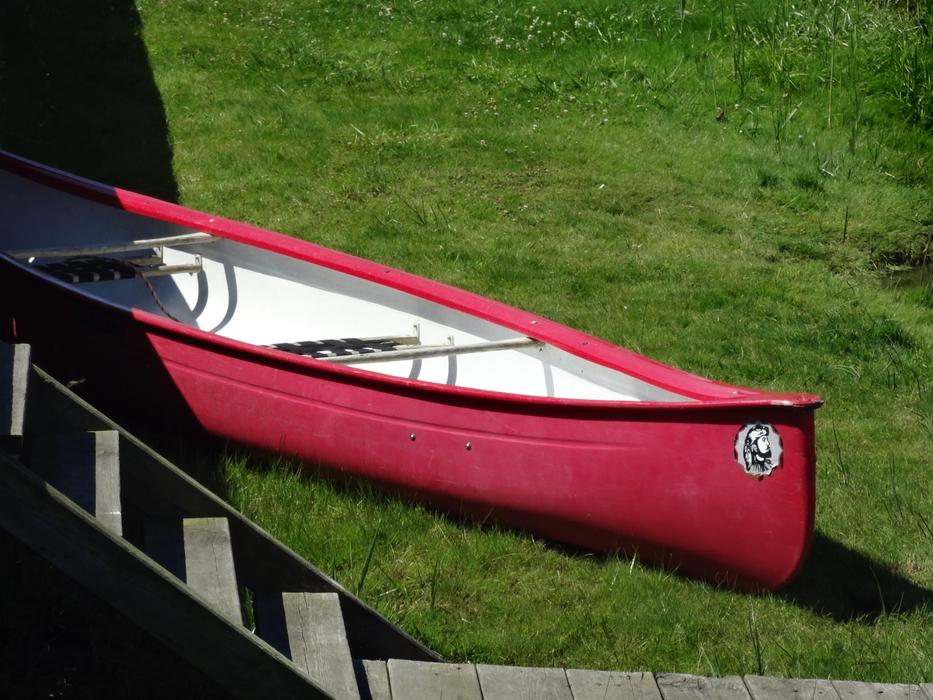 Red and white boat on the green grass near the stairs, in sunlight
