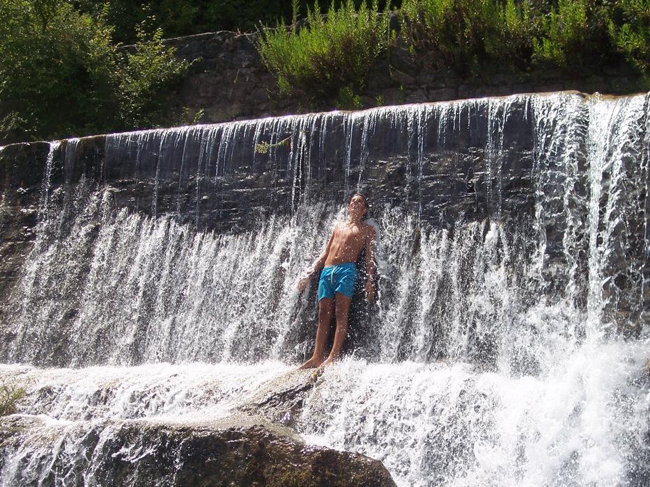 Guy standing in the beautiful waterfall, on the rocks, near the colorful plants