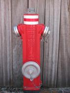 Red, white and metallic water hydrant near the wooden wall
